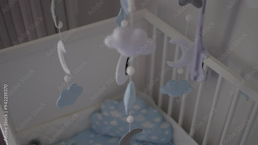 Baby mobile with clouds and moons hangs over a white crib with blue bedding. Baby mobile with clouds and moons hangs over a white crib with blue bedding.