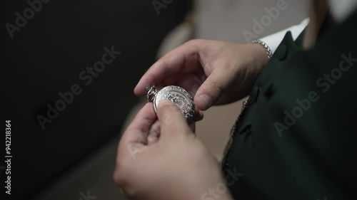 Hands holding a silver pocket watch, carefully examining the intricate details