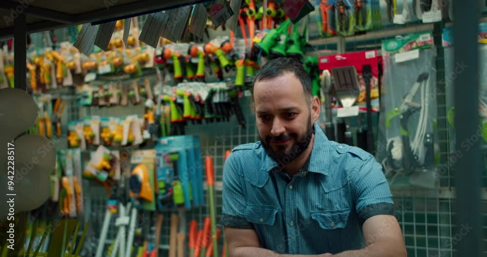 A confident brunette man with a beard in a blue shirt examines goods on the shelves in a garden store A confident brunette man with a beard in a blue shirt examines goods on the shelves in a garden store