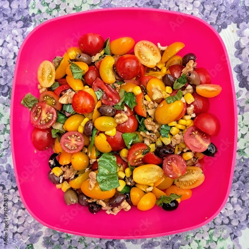 Mixed salad vegetables consisting of a red and yellow tomatoes, basil parsley walnuts corn celery. Fresh summer vegetables to eat as a side dish or as a main course. Table with purple floral tableclot photo