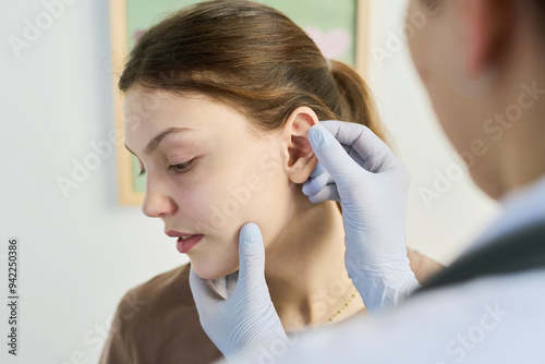 Medical professional wearing gloves examining patient's ear during ear check-up in clinic focusing on detail. Close-up shot of medical procedure in sterile environment photo