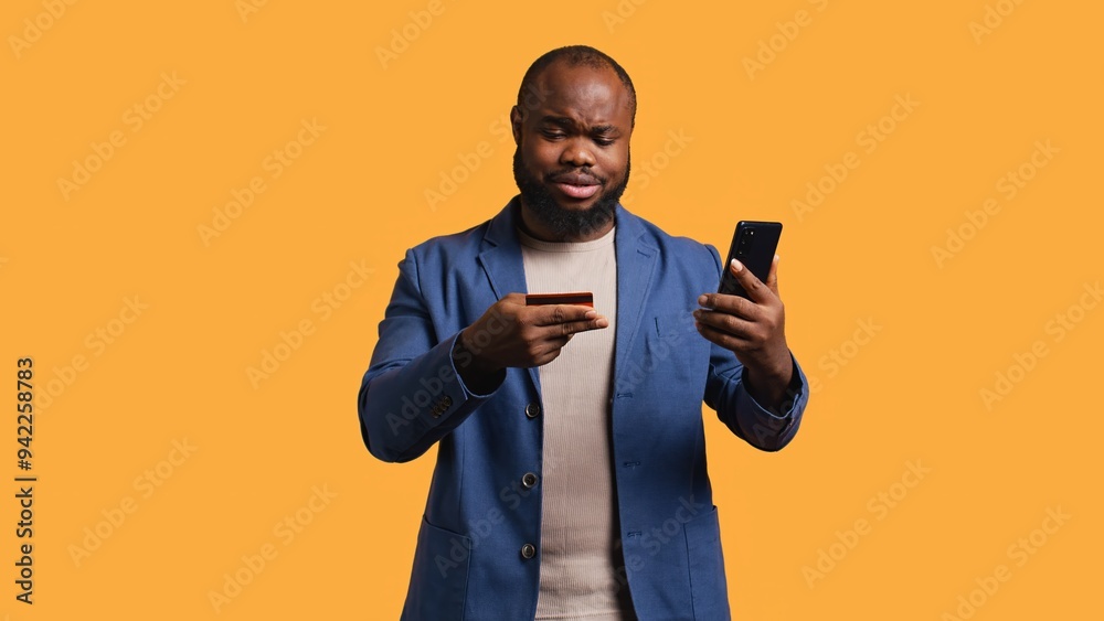 Man upset after lacking necessary money while trying to buy stuff online on smartphone. Sad person looking at debit card after getting transaction rejected on phone, studio background, camera B Man upset after lacking necessary money while trying to buy stuff online on smartphone. Sad person looking at debit card after getting transaction rejected on phone, studio background, camera B