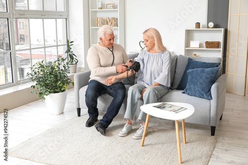 Mature man measuring blood pressure of his wife at home