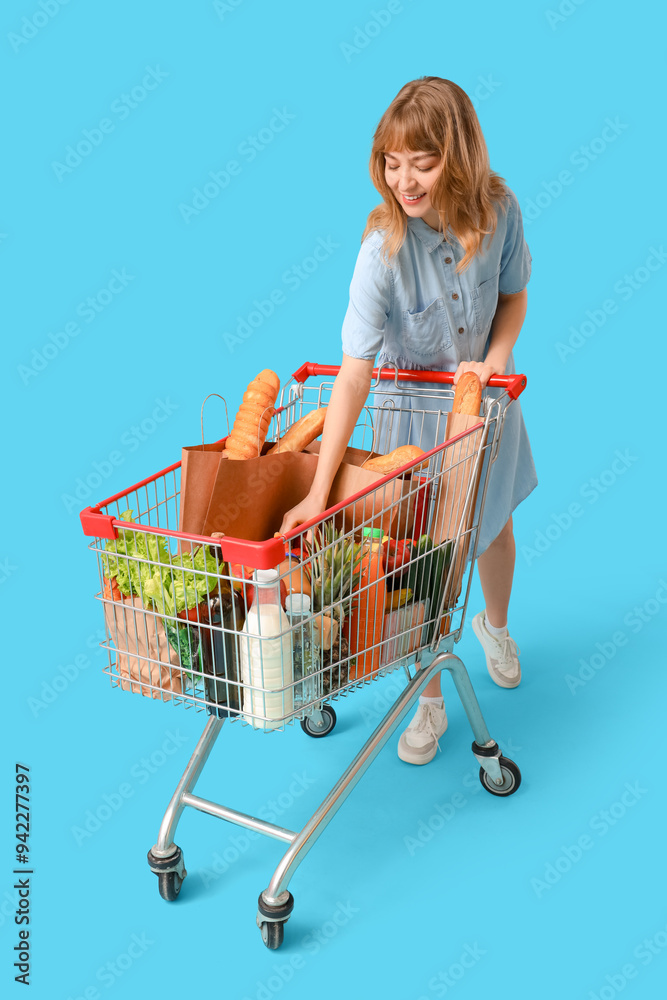 Young woman with full shopping cart on blue background Young woman with full shopping cart on blue background
