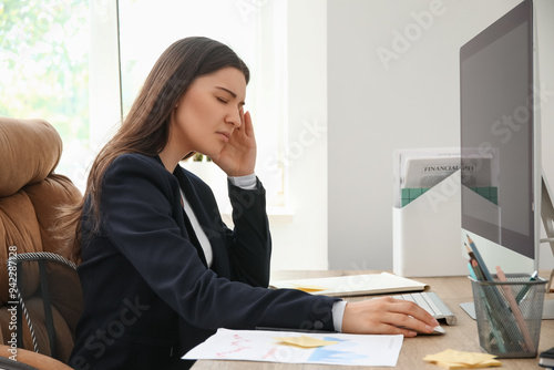 Young woman suffering from headache while working with modern computer at workplace in office