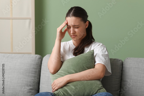 Young woman suffering from headache and sitting on sofa at home