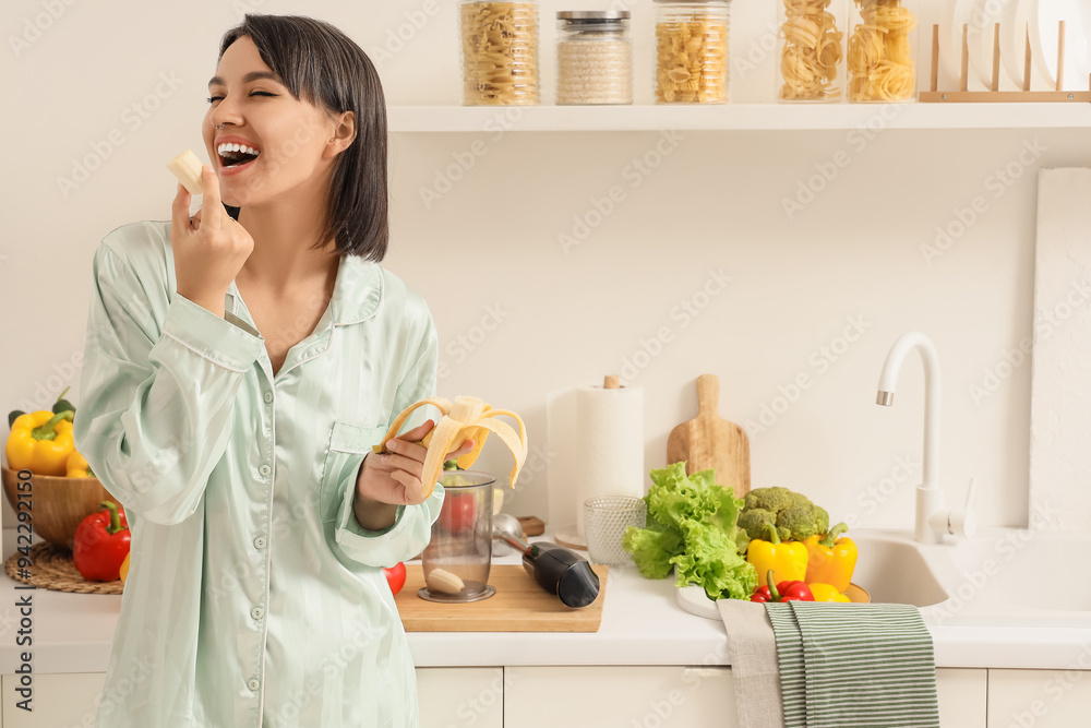 Young woman with blender eating banana in kitchen Young woman with blender eating banana in kitchen