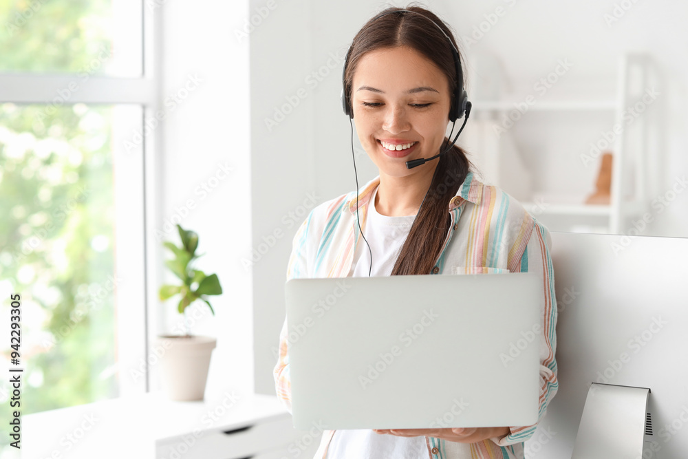 Young female receptionist in headset with modern laptop in office Young female receptionist in headset with modern laptop in office