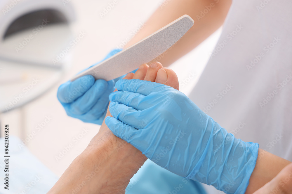 Young man getting professional pedicure with file on couch in spa salon, closeup Young man getting professional pedicure with file on couch in spa salon, closeup