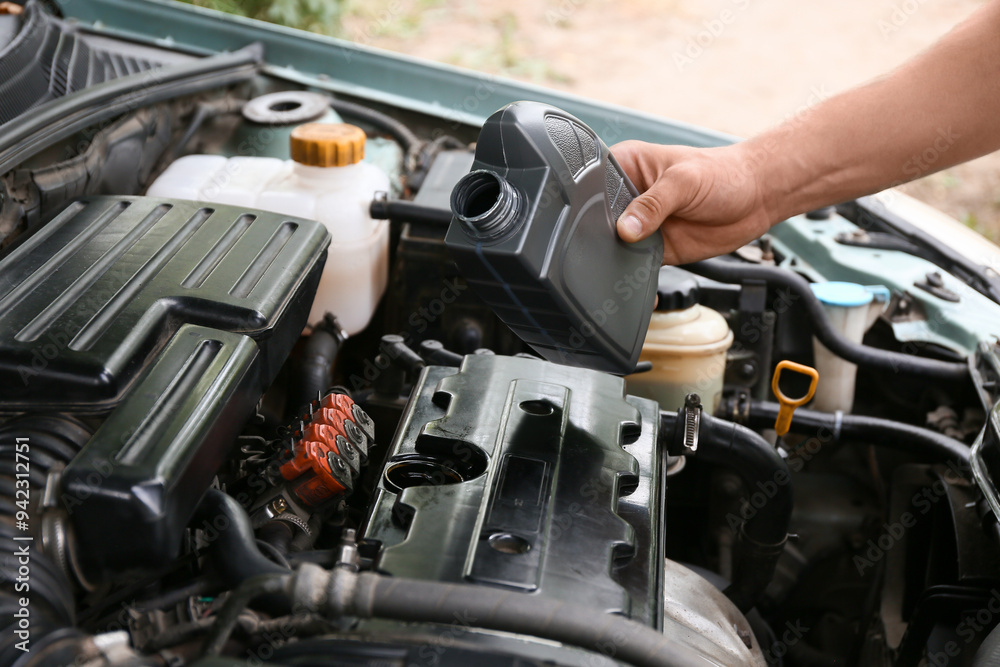 Male mechanic pouring car oil into engine outdoors, closeup Male mechanic pouring car oil into engine outdoors, closeup