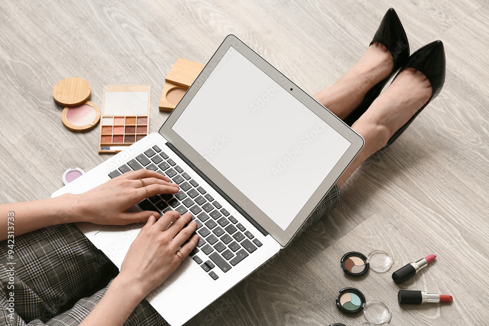 Fototapeta premium Makeup artist with cosmetic products using laptop on wooden floor, closeup