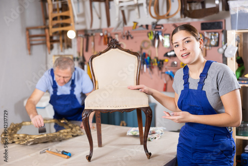 Young female master restoration worker dressed in overalls poses in working atmosphere of his workshop after working with antique furniture photo