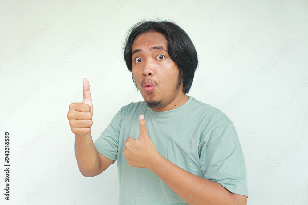 Excited and happy long haired Asian man gives thumbs up hand gesture of approval, isolated by gray background. Excited and happy long haired Asian man gives thumbs up hand gesture of approval, isolated by gray background.