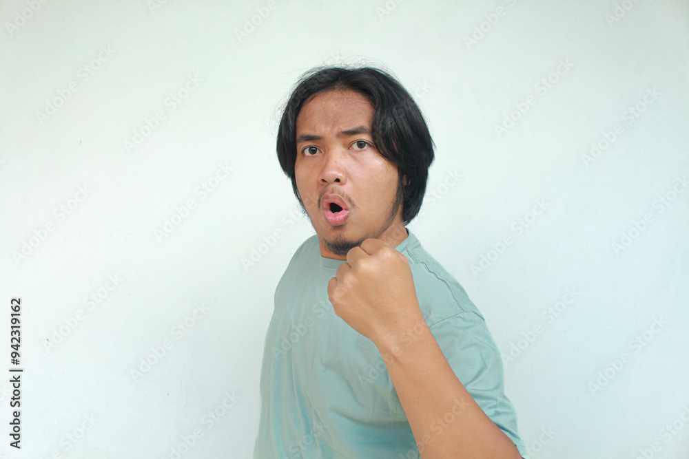 Happy excited and smiling long haired young Asian man raising his arm up and and scream to celebrate success or achievement. Isolated in gray background. Happy excited and smiling long haired young Asian man raising his arm up and and scream to celebrate success or achievement. Isolated in gray background.