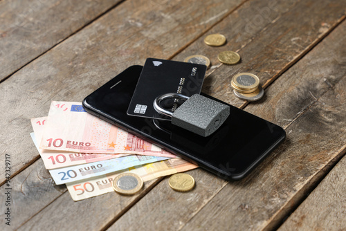 Mobile phone with padlock, credit card and money on wooden background, closeup. Cyber security concept