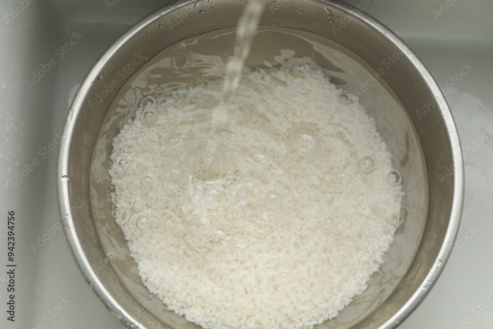 Pouring water into bowl with rice in sink, top view Pouring water into bowl with rice in sink, top view
