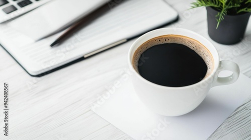 A minimal workspace setup featuring a coffee cup, a laptop, and a notepad on a white desk with a small potted plant..