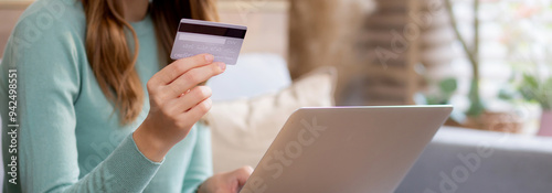 Young asian woman sitting on sofa using laptop computer shopping online with credit card buying to internet, female payment with business on couch, purchase and payment, business and lifestyles.