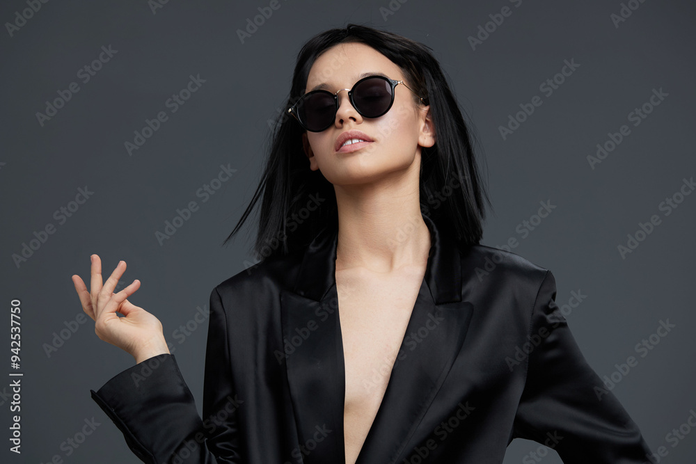 Businesswoman in black suit and sunglasses confidently posing against a gray background, exuding elegance and modern style, perfect for corporate and fashion themes Businesswoman in black suit and sunglasses confidently posing against a gray background, exuding elegance and modern style, perfect for corporate and fashion themes