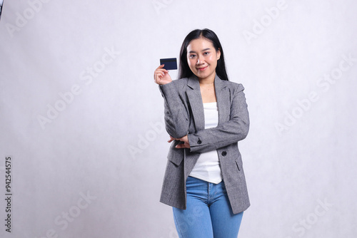 portrait of beautiful young office lady asia smiling holding debit credit atm card wearing grey suit standing isolated on white background. for corporate, lifestyle, finance, transaction content photo