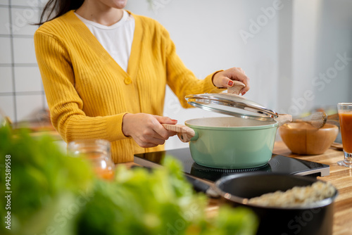 A close-up image of a woman is cooking in the kitchen, opening a pot lid to check her soup.