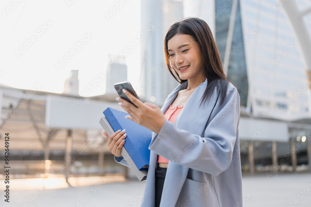 Asian businesswoman using mobile phone device while standing in city. Asian businesswoman using mobile phone device while standing in city.