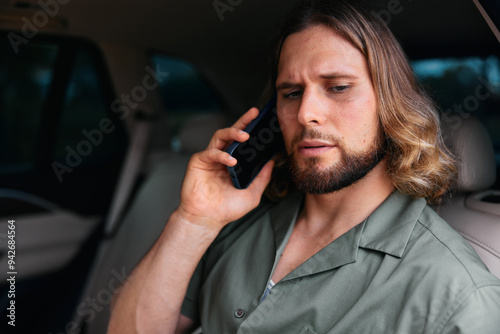 Man in a car talking on the phone with a serious expression, wearing a green shirt, seated in a modern vehicle interior