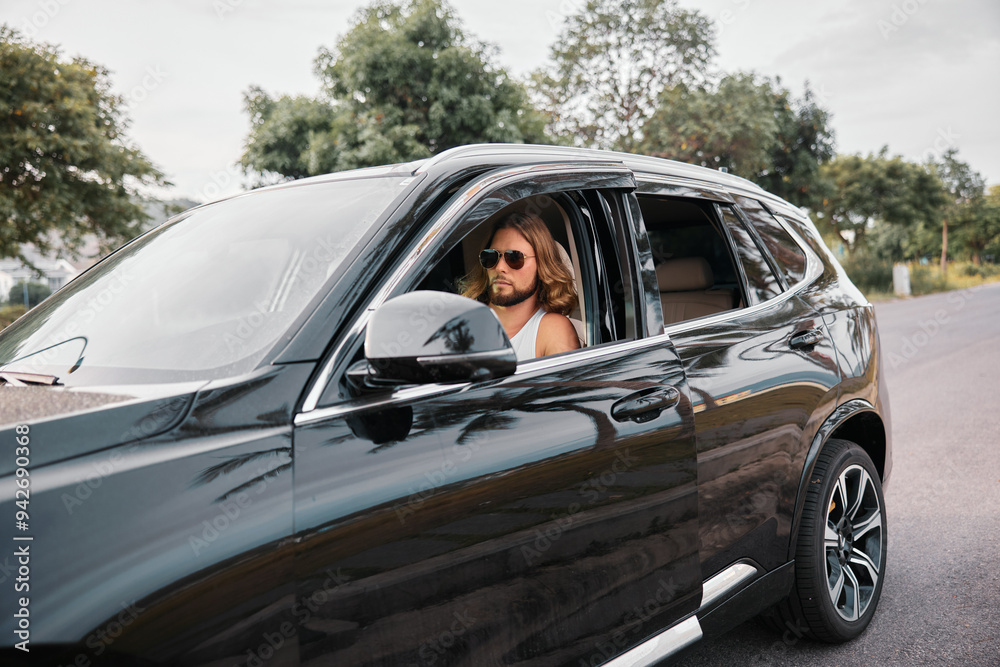 Stylish man with sunglasses driving a black SUV on a scenic road surrounded by greenery Stylish man with sunglasses driving a black SUV on a scenic road surrounded by greenery