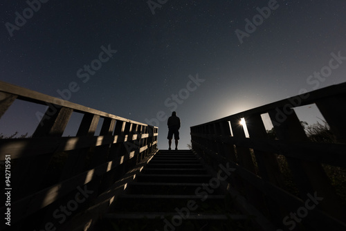 Night scene, silhouette of a hooded man on a staircase in nature under moonlight and starry sky. photo