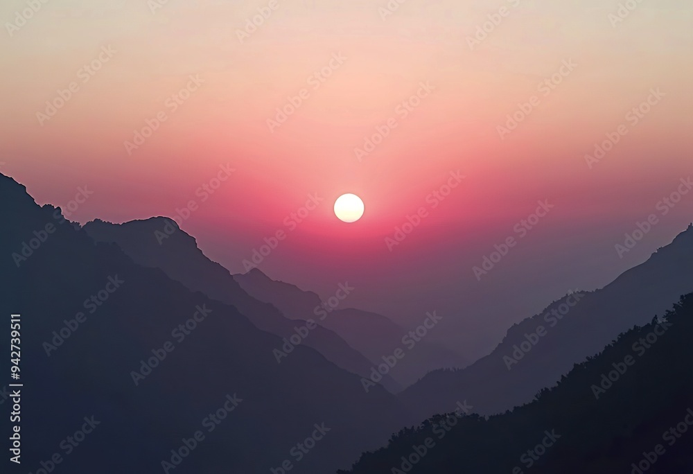 A large pink sun setting over a silhouetted mountain range against a pale sky A large pink sun setting over a silhouetted mountain range against a pale sky