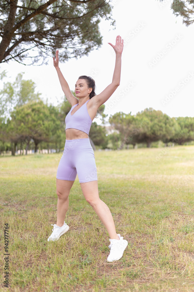 A Young Woman Energetically Performing Jumping Jacks in a Beautiful Park Bathed in Sunlight on a Warm, Sunny Day A Young Woman Energetically Performing Jumping Jacks in a Beautiful Park Bathed in Sunlight on a Warm, Sunny Day