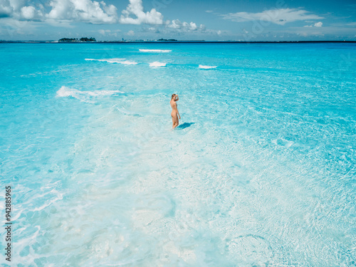 Woman in swimsuit staying on tropical white sandy beach with turquoise ocean water. Drone view