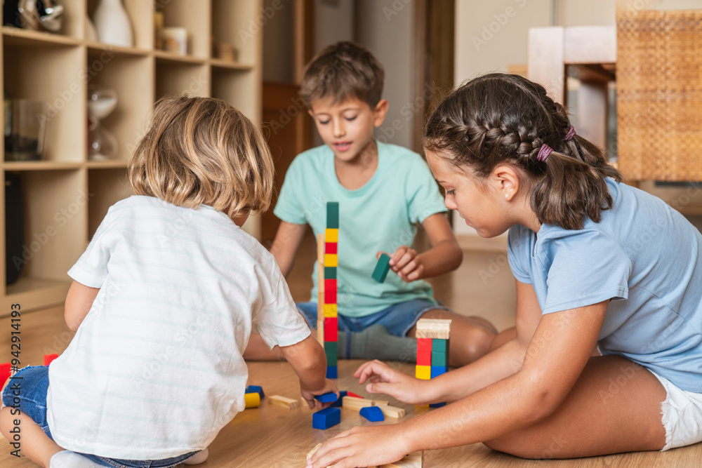 Childhood At Home: Three Children Happily Playing Together On A Floor, Enjoying A Creative Game With Wooden Blocks. Concept Of Family And Education. Childhood At Home: Three Children Happily Playing Together On A Floor, Enjoying A Creative Game With Wooden Blocks. Concept Of Family And Education.