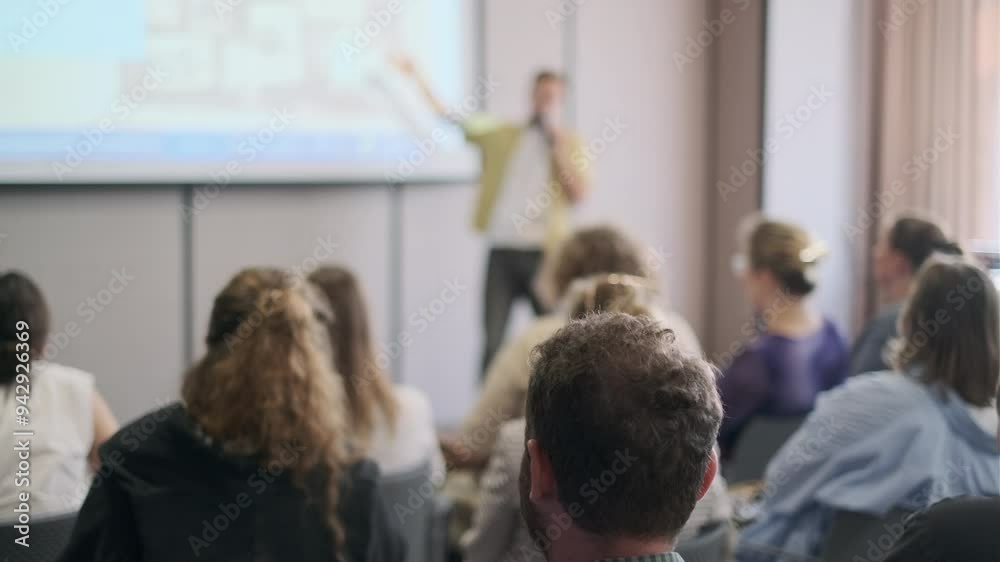 Group of people engaged in a presentation, focusing on the speaker delivering information in a conference setting.
