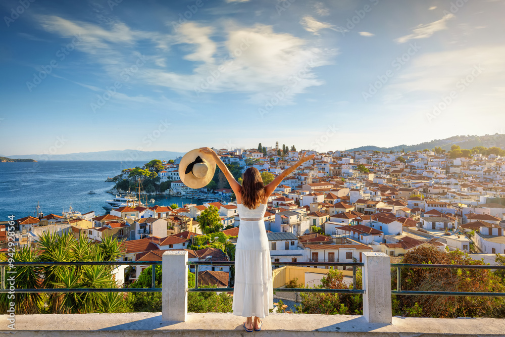 A happy tourist woman enjoys the beautiful summer sunset view of the town of Skiathos island, Sporades, Greece