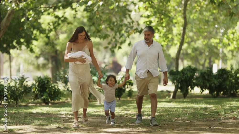 Joyful family enjoying a sunny stroll in the park with their toddler and newborn baby Joyful family enjoying a sunny stroll in the park with their toddler and newborn baby
