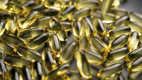 Yellow Omega-3 fish oil softgel capsules falling on a grey plate. Translucent supplements with unsaturated fatty acids. Slow motion. Macro shot. Healthy lifestyle concept