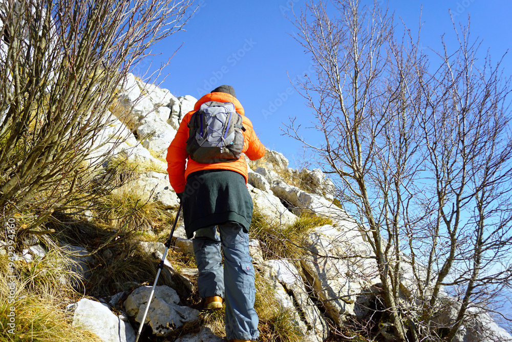 A man walking along a mountain route on the coast of Montenegro. A tourist in a bright jacket with a backpack and hiking poles climbs to the top of Radostak on Mount Orjen. Herceg Novi - winter hiking A man walking along a mountain route on the coast of Montenegro. A tourist in a bright jacket with a backpack and hiking poles climbs to the top of Radostak on Mount Orjen. Herceg Novi - winter hiking