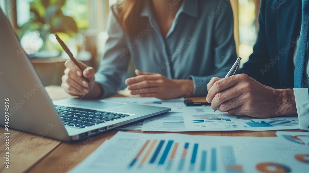 Two business leaders, a middle-aged man and woman, collaborate on a laptop, reviewing financial documents and engaging in a discussion.