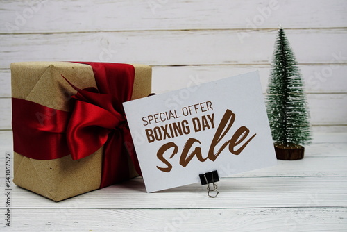 Boxing day Sale text on paper card with gift box and artification pine tree on wooden background photo