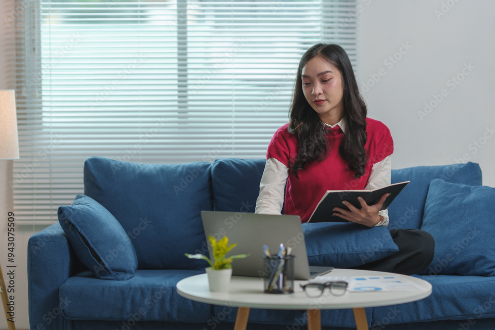Beautiful Asian woman collecting data Study online or take notes in a notebook while sitting on the sofa in her living room. Concept of relaxation Working on holidays. Beautiful Asian woman collecting data Study online or take notes in a notebook while sitting on the sofa in her living room. Concept of relaxation Working on holidays.