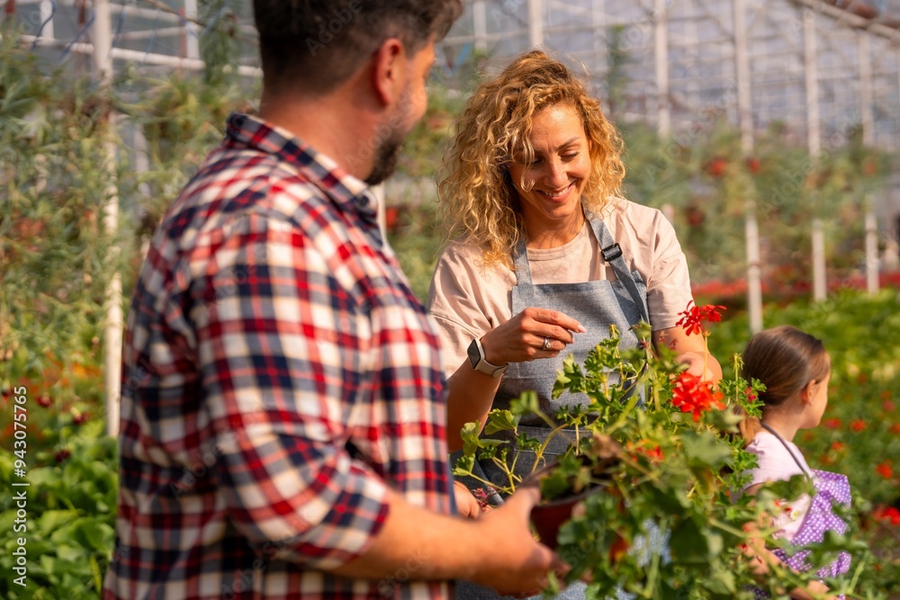 The owners of a small family flower nursery discussing plant care, surrounded by their lush, vibrant greenhouse.