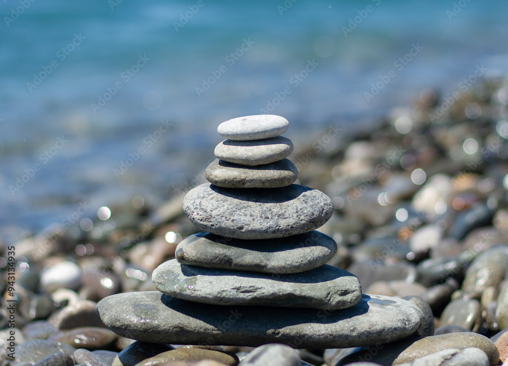 Balanced pebble pyramid silhouette on the beach with the sea