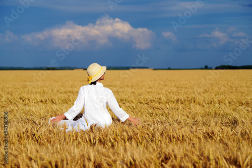 Young beautiful woman in a white dress on a Golden wheat field admiring the harvest.