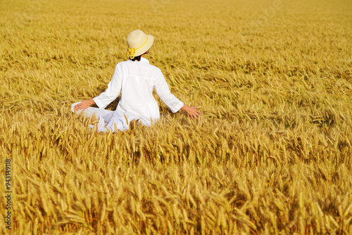 Young beautiful woman in a white dress on a Golden wheat field admiring the harvest.