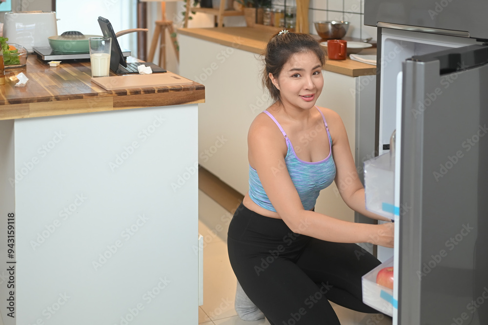 Young asian woman wearing a sportswear picking something from a fridge Young asian woman wearing a sportswear picking something from a fridge