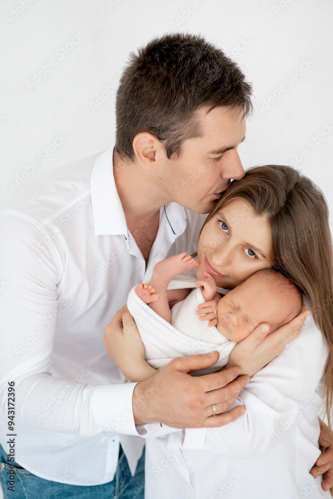 young parents with a newborn baby hug and kiss, happy mom and dad admiring the baby at home on the bed, a happy family caring for a small child, a place for text young parents with a newborn baby hug and kiss, happy mom and dad admiring the baby at home on the bed, a happy family caring for a small child, a place for text