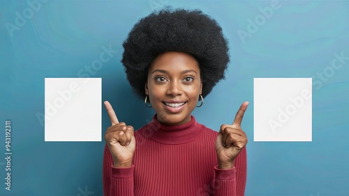 A pleased dark-skinned woman with an Afro hairstyle, pointing with both forefingers to empty space for your promotion, against a blue background.