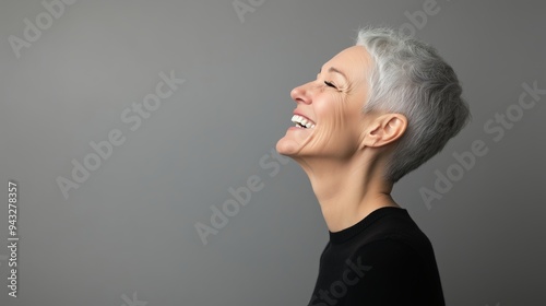 A joyful woman with short gray hair laughing against a neutral backdrop, capturing a moment of happiness and spontaneity