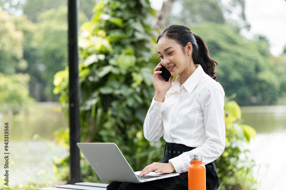 Young Professional Woman Working Outdoors on Laptop and Talking on Phone in a Park Setting Young Professional Woman Working Outdoors on Laptop and Talking on Phone in a Park Setting